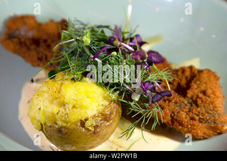 Ein Käse mit Marmorplatten gebackene Kartoffel mit einem Frittiertes Fischfilet serviert, in einer Jacke für Breadcrumbs aus. Stockfoto