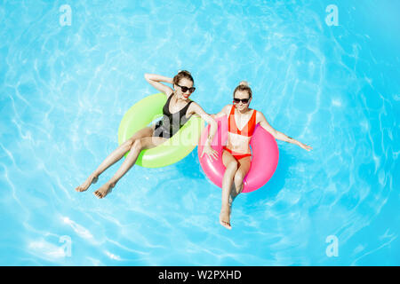 Zwei Frauen schwimmen auf der aufblasbaren Ringen, entspannen im Pool im Freien während des Sommers, Ansicht von oben Stockfoto