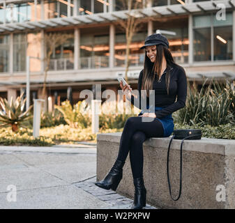 Modische junge Frau mit Sling Bag an ihrer mo Suchen sitzen Stockfoto