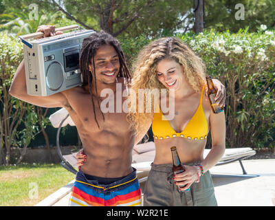 Interracial Paare, schwarzer Mann und kaukasische Frau zu Fuß mit einer Kassette Radio am Pool Stockfoto