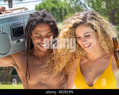 Interracial Paare, schwarzer Mann und kaukasische Frau zu Fuß mit einer Kassette Radio am Pool Stockfoto