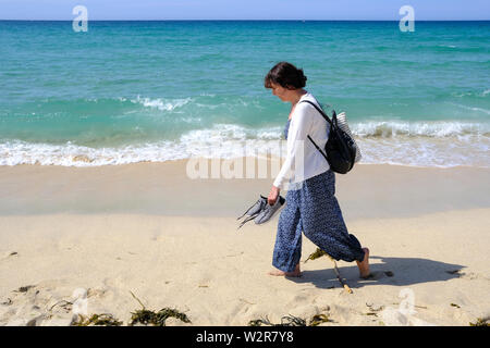 Eine Frau, die zu Fuß entlang der Küste an einem schönen Strand in St Ives in Cornwall. Stockfoto