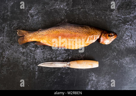 Hohen Winkel in der Nähe von One frisch geräucherte ganze Forellen und ein Messer auf schwarzem Schiefer. Stockfoto