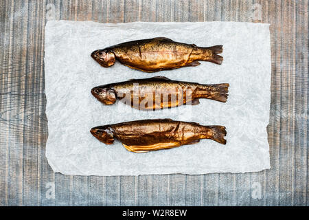 Hohen Winkel in der Nähe von drei frisch geräucherte ganze Forelle auf weißem Papier. Stockfoto