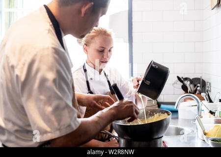 Männliche und weibliche Chef tragen braune Schürze an der Theke stehend, die Sauce Hollandaise. Stockfoto