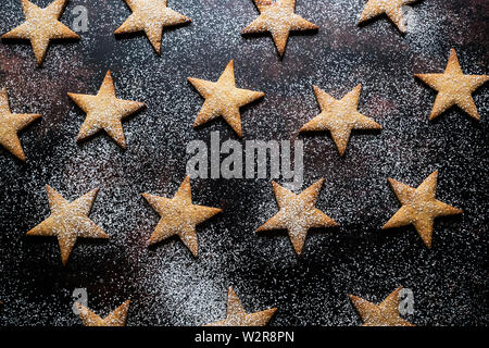 Hohen Winkel in der Nähe von frisch gebackenen sternförmige Plätzchen mit Puderzucker auf schwarzem Hintergrund entstaubt. Stockfoto