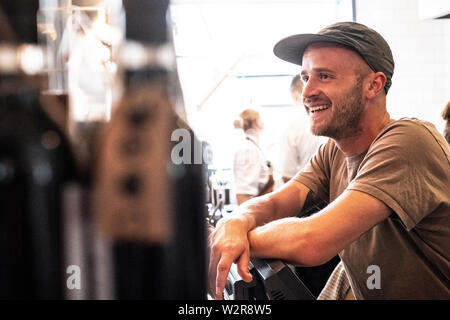 Portrait von bärtigen Mann mit Baseball Cap in einem Cafe stehend, lächelnd. Stockfoto