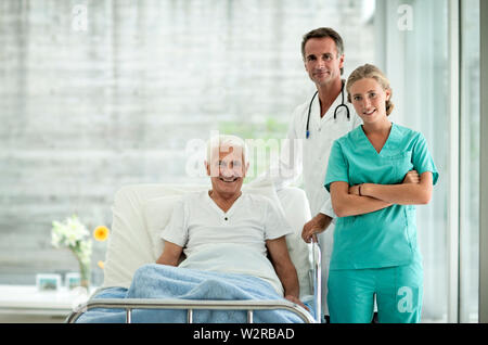 Portrait von älteren Mann im Krankenhaus, Bett, ein Arzt und eine Krankenschwester neben ihm. Stockfoto
