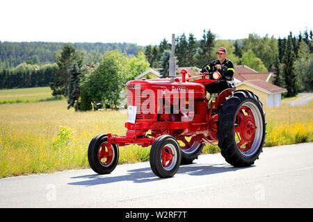 Kimito, Finnland. Juli 6, 2019. Man treibt rot International Harvester Farmall M Traktor, Jahr 1951, auf die kimito Tractorkavalkad, vintage Traktor Parade. Stockfoto