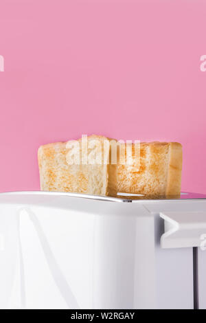 Getoastetes Toast Brot im Toaster weiß auf rosa Hintergrund Stockfoto
