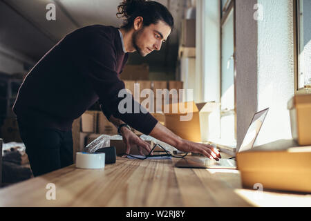 Junger Mann bei der Arbeit auf dem Laptop, nachdem die Dichtung das Paket für die Lieferung. Inhaber kleiner Unternehmen arbeiten im Büro. Stockfoto