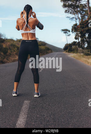 Rückansicht der jungen Frau, die auf eine leere Straße fertig, für einen Lauf. Sportliche Frau bereit für Ihren morgendlichen Workout. Stockfoto