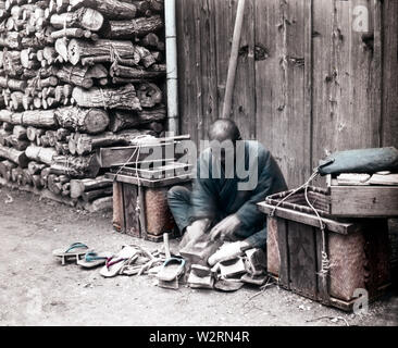 [1890s Japan - Geta verstopfen Handwerker] - Geta Handwerker bei der Arbeit auf der Straße. Geta Handwerker um, ihre Dienstleistungen in der Reparatur von Geta ging, Holz- Schuhwaren. Tools wie ein Beil, Flugzeug, und Meißel wurden in Körben auf einer Stange ausgeglichen. 19 Vintage Glas schieben. Stockfoto