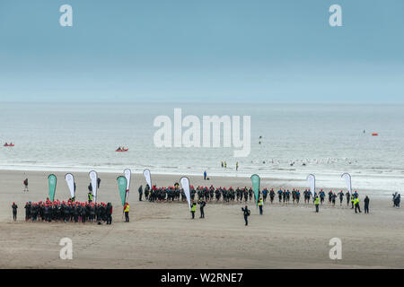 Unter dunklen Wolken, die Wettbewerber im Jahr 2019 Barry Island sprint Triathlon über den sandigen Strand und ins Meer zu Beginn des Rennens. Stockfoto