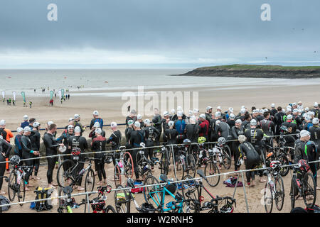 Unter dunklen Wolken, die Wettbewerber im Jahr 2019 Barry Island sprint Triathlon warten auf der Promenade neben dem Strand von ihrer Rasse zu starten. Stockfoto