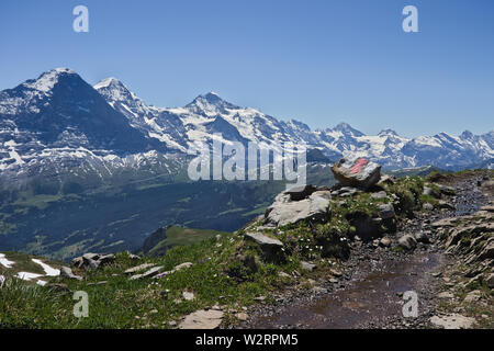 Wanderweg Zeichen (weiß rot weiße Streifen) auf einem Felsen neben dem Wanderweg mit Bergen (Eiger, Mönch und Jungfrau) im Hintergrund. Stockfoto