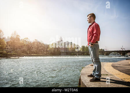 Nachdenklicher junger Mann, der am Fluss in Turin sitzt Stockfoto