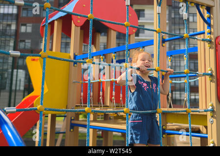 Teenager versuchen, Klettern am Seil an der Wand. Sie spielt mit dem Seil an der Wand die motorische Aktivität auf dem Spielplatz zu entwickeln. Stockfoto