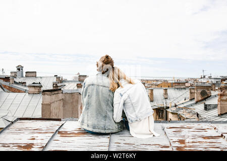 Ein junges Paar sitzt auf dem Dach bewundert und einer schönen Aussicht auf die Stadt. Romantik, Liebe und vertrauensvolle Beziehungen. Oder er Traum oder digital detox zusammen. Stockfoto