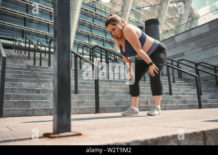 Killing Workout. Müde junge plus size Frau in Sportkleidung Gefühl müde nach dem Training, während im Freien stehen. Gesundes Leben. Sportkonzept. Abnehmen. Stockfoto