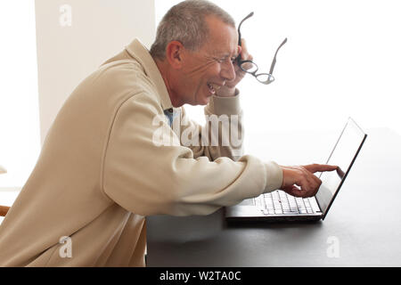 Ein Mann sitzt laut lachend mit offenen Mund, als er auf dem Bildschirm eines Notebooks punkten. Er liest oder sieht etwas sehr lustig auf dem Bildschirm. Halten Stockfoto