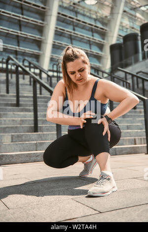 Schmerzen nach dem Training. Junge Übergrößen Frau berühren Ihr Knie und Schmerzen nach dem Sport Training beim Stehen auf Treppen. Sportverletzung. Gewicht zu verlieren. Stockfoto