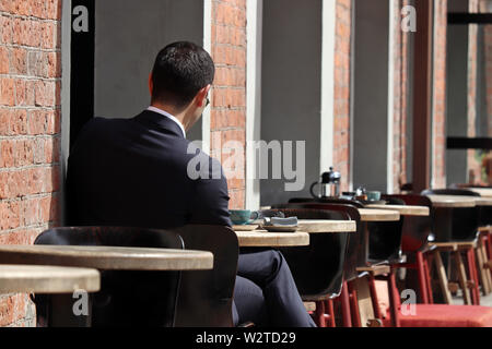 Stilvolle Mann in einen Anzug an einem Tisch sitzen in Street Cafe. Konzept der Mittagessen allein, Warten auf ein Datum oder eine geschäftliche Besprechung, Kaffeepause Stockfoto