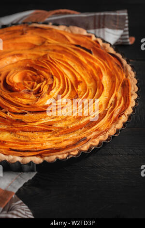 Bild vertikal mit Süßkartoffel tart in Rose Blume Form, auf einem schwarzen Holztisch. Herbst, schmackhaftes Essen. Rustikale Bild mit amerikanischen Torte. Stockfoto