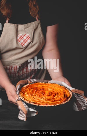 Frau mit Schürze, die eine traditionelle amerikanische Süßkartoffel-Torte, in Form einer Blume, frisch gebackene, über eine rustikale schwarz Tisch. Thanksgiving Essen. Stockfoto