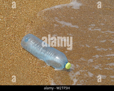 Kunststoff Flasche im Sand am Strand mit Wellen im Hintergrund, Konzept der Meeresverschmutzung durch Abfälle aus Kunststoffen Stockfoto