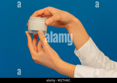 Woman's Hände, die kosmetische Creme Container auf Blau Stockfoto