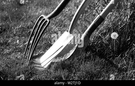 Eine Gartenarbeit Gartenarbeit Gabel einen Spaten und eine Gartenbau Schaufel gegeneinander gelehnt von Grass in einem Garten umgeben, schwarz-weiß Foto, Hori Stockfoto