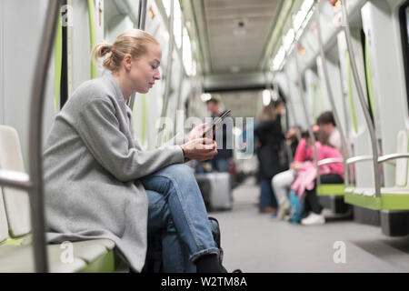 Schöne blonde Frau mit Mobiltelefon während der Fahrt mit der U-Bahn mit den öffentlichen Verkehrsmitteln. Stockfoto
