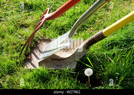 Eine rote Gartenarbeit Gartenarbeit Gabel einen Spaten und eine Gartenbau Schaufel mit einem gelben Griff lehnte sich gegen jede andere von Grass in einem Garten umgeben, Horizon Stockfoto