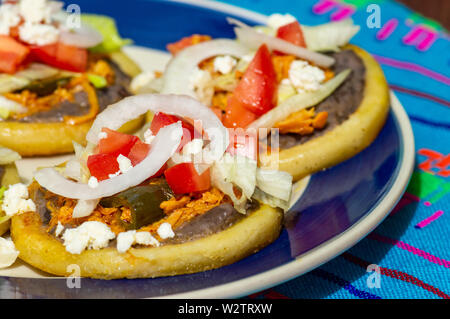 Mexikanische sopes gemacht mit Huhn tinga, Chilis, schwarz refried Beans und frische Zwiebel, Salat und Tomaten Stockfoto