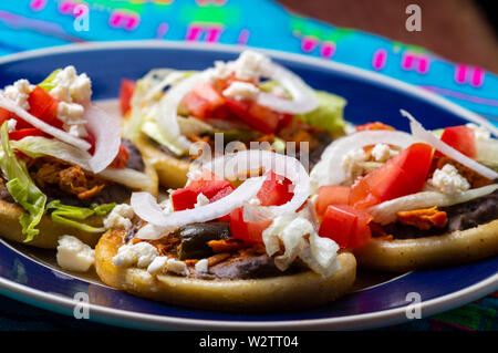 Mexikanische sopes gemacht mit Huhn tinga, Chilis, schwarz refried Beans und frische Zwiebel, Salat und Tomaten Stockfoto