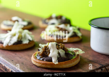 Mexikanische vegetarische sopes mit schwarzen refried Beans und frische Zwiebeln und Salat gemacht, garniert mit Sahne und grüne Salsa Stockfoto