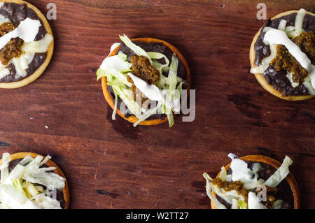 Mexikanische vegetarische sopes mit schwarzen refried Beans und frische Zwiebeln und Salat gemacht, garniert mit Sahne und grüne Salsa Stockfoto