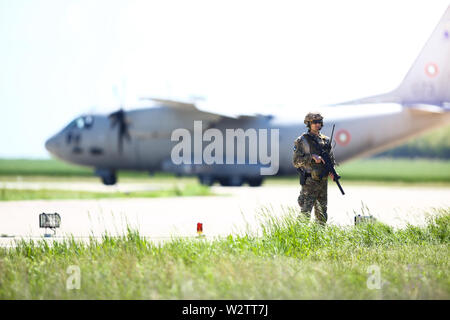 Boboc, Rumänien - 22. Mai 2019: Die rumänische Armee Soldat Patrouillen ein Military Air Base, mit einem Alenia C-27J Spartan militärischen Frachtflugzeug aus der Bulgarischen Stockfoto