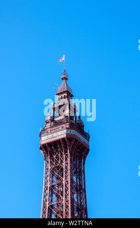 Die obere Hälfte der Blackpool Tower gegen einen strahlend blauen Himmel mit Aussichtsplattform Crows Nest und Flagge auf der Oberseite Stockfoto