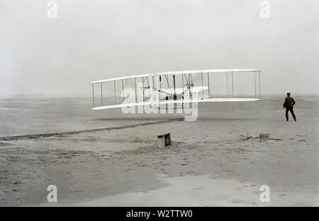 Ersten erfolgreichen Flug der Gebrüder Wright Flyer, die durch die Brüder Wright. Die Maschine reisten 120 ft (36,6 m) In 12 Sekunden um 10:35 Uhr in Kitty Hawk, North Carolina. Orville Wright war an die Bedienelemente der Maschine, liegend anfällig auf der unteren Tragfläche mit seinen Hüften in der Wiege, die den Flügel - warping Mechanismus betrieben. Wilbur Wright lief entlang der Maschine auszugleichen, und nur seinen Einfluß auf die vordere Strebe der rechten in das Foto veröffentlicht. Die Rampe, die Flügel - Rest, eine Spule, und andere Elemente für die Flugvorbereitung notwendig sind sichtbar hinter der Maschine. Dies wurde als f Stockfoto