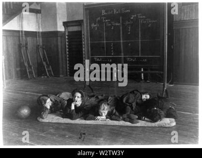 Fünf Mädchen liegen auf Matten in der Turnhalle vor Basketball scoreboard Stockfoto