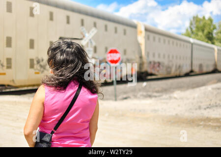 Eine Frau in einer rosa Bluse wartet in der heißen Sonne als ein Zug die Gleise vor ihr Im inländischen Nordwesten der Vereinigten Staaten von Amerika durchquert. Stockfoto