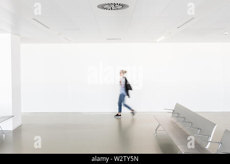 Bewegungsunschärfe einer Frau, die in einem modernen weißen leeren Flur läuft Stockfoto