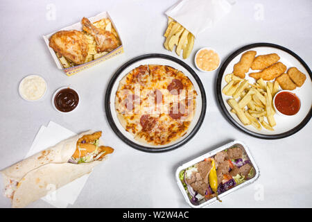 Auswahl an ungesunden Take Way Fast-Food präsentiert auf dem Tisch mit weißem Papier bedeckt. Pizza, Pommes, Chicken Nuggets, Kebab. Stockfoto