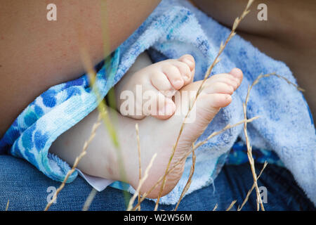 Nahaufnahme eines Babys Bein in einem blauen Handtuch unter ihrer Mütter Knie liegend, selektiver Fokus Stockfoto