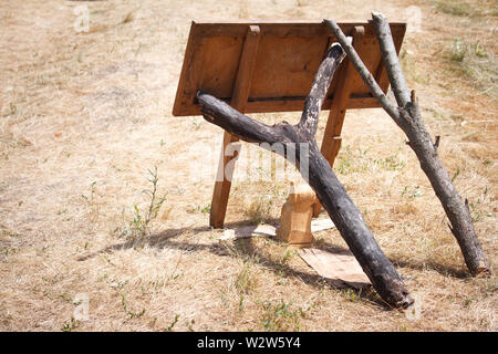 Holz- Wegweiser fällt und zwei knorrige Äste Unterstützung, die es vor dem Hintergrund der verdorrten Gras. Stockfoto