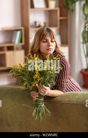 Schöne junge Frau mit Blumenstrauß von Mimosa Blumen zu Hause Stockfoto