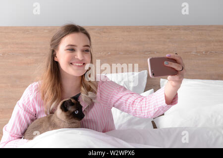 Junge Frau von selfie mit niedlichen Siamesische Katze im Schlafzimmer Stockfoto