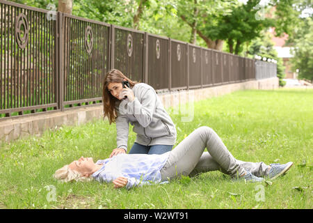 Weibliche Passanten Aufruf ein Krankenwagen für unbewusste reife Frau im Freien Stockfoto